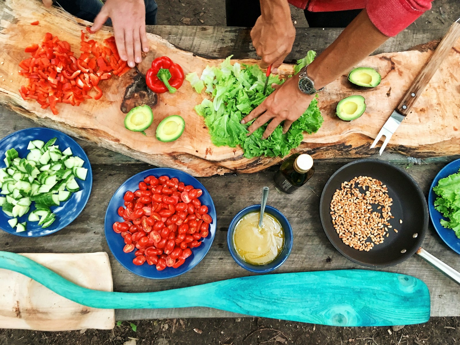 Hands slicing fresh green vegetables beside plates of colourful salad
