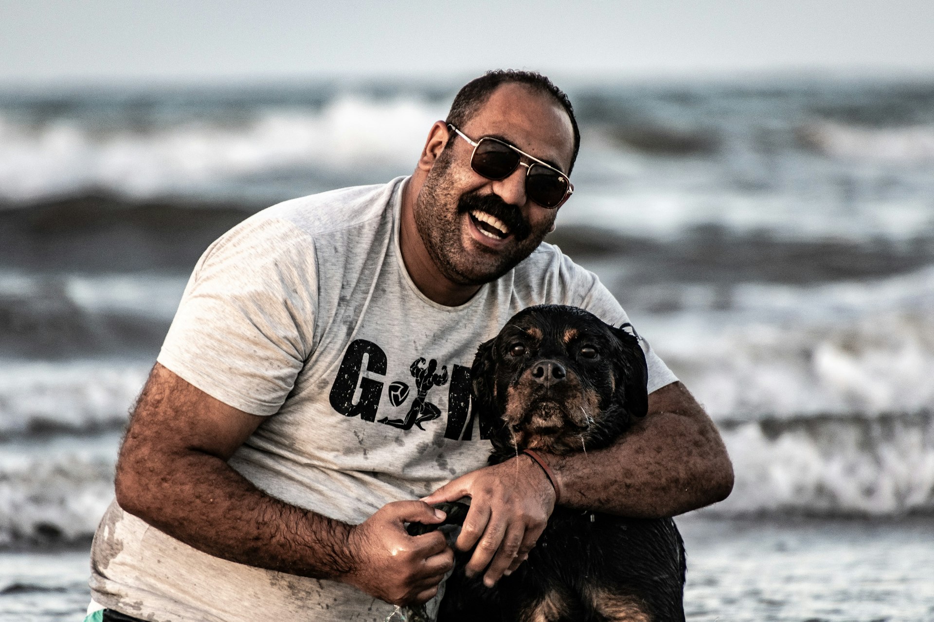 A man laughing as he hugs his dog on the beach