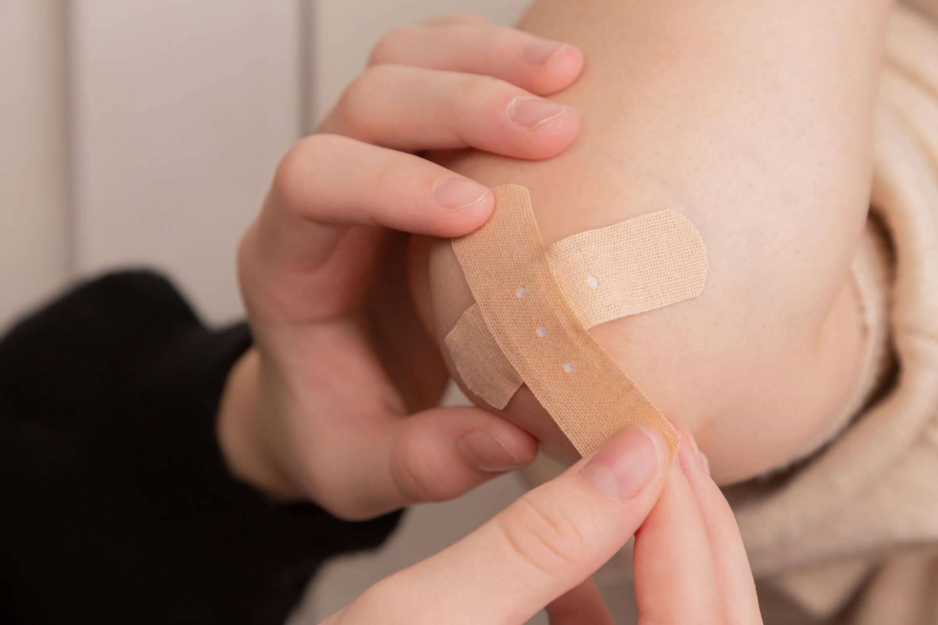 Hands gently placing a small plaster on a child’s skin