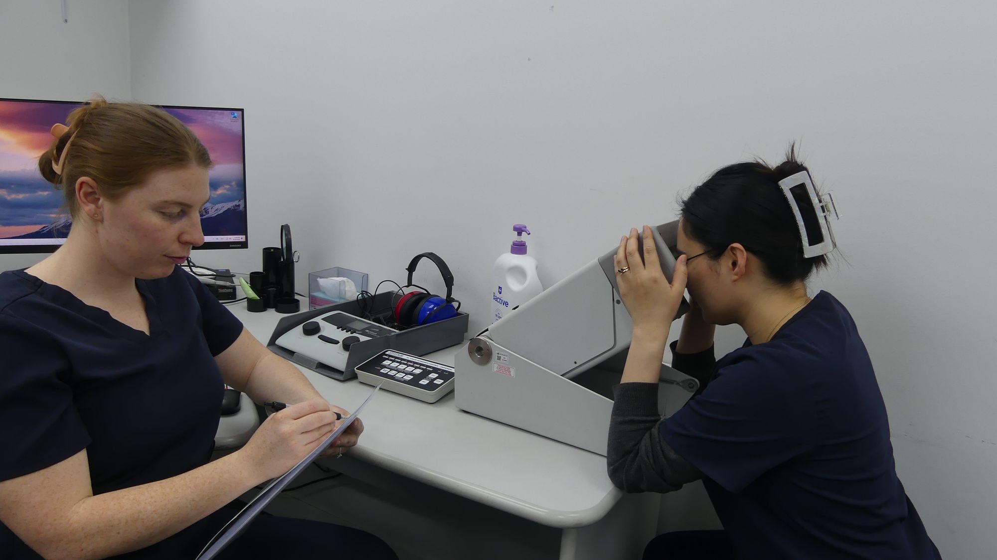 A patient at the vision screener while nurse Maddy records the results