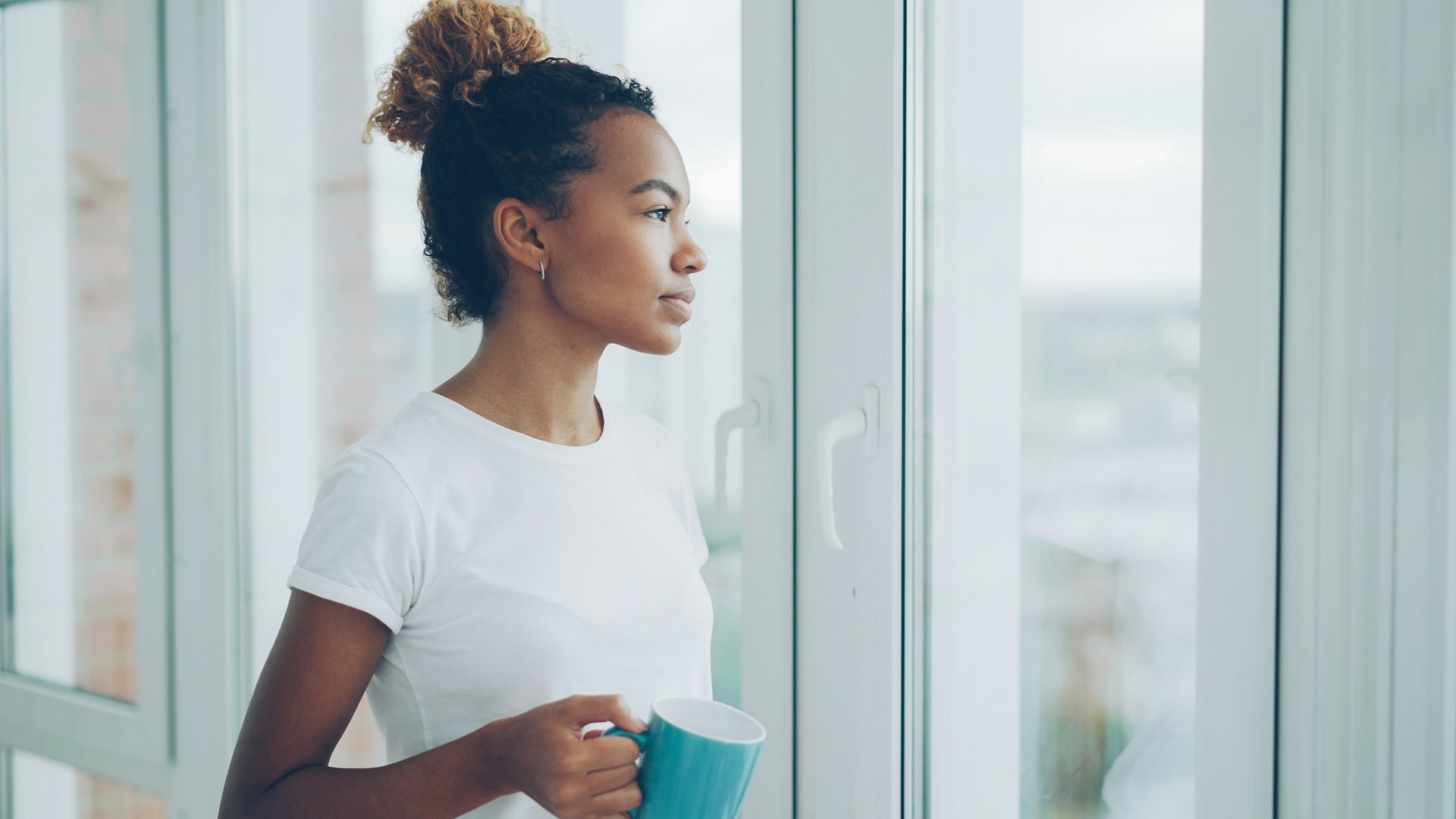 A woman with a cup of tea relaxing by a sunny window